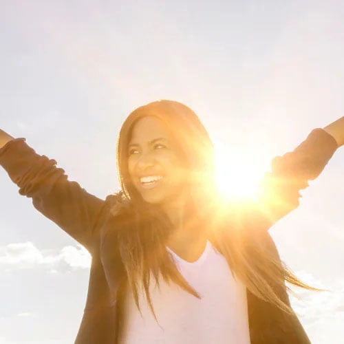 Happy Model in the sunshine with arms raised.